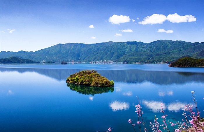 泸沽湖的美，是无法用语言描述的。倘佯泸沽湖边，没有一点杂念，唯有让心灵尽情感受，感受上苍赐予的美。湖边青草葱翠，密密匝匝，不沾一粒尘埃。平静的湖水，倒映湖岸延绵起伏的山丘，闪烁耀眼的银光，湖里的白云，似雪莲绽放。从湖底生出的水草，柔柔地漂荡，水草间，不时有小鱼儿穿梭往来。散落在湖边的，那些摩梭族人居住的木屋，没有一点刻意的布局，却与这环境是那么协调，好似自然天成一般。