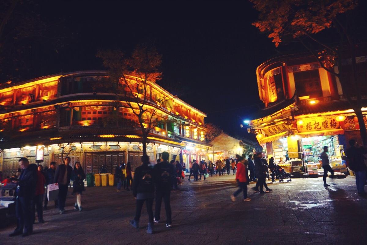 黄色的灯光勾勒出不同风格的建筑，有的简朴端庄，有的用它宫殿式的挑脚呈现出它的高贵。屋檐下亮着造型各异的灯笼，长长的灯穗在晚风中舞动。一棵大树亮着点点白光，远远望去犹如一树盛开的梨花，游人围坐在它的树荫下，聊天观看夜景，享受古城独特魅力的夜景。